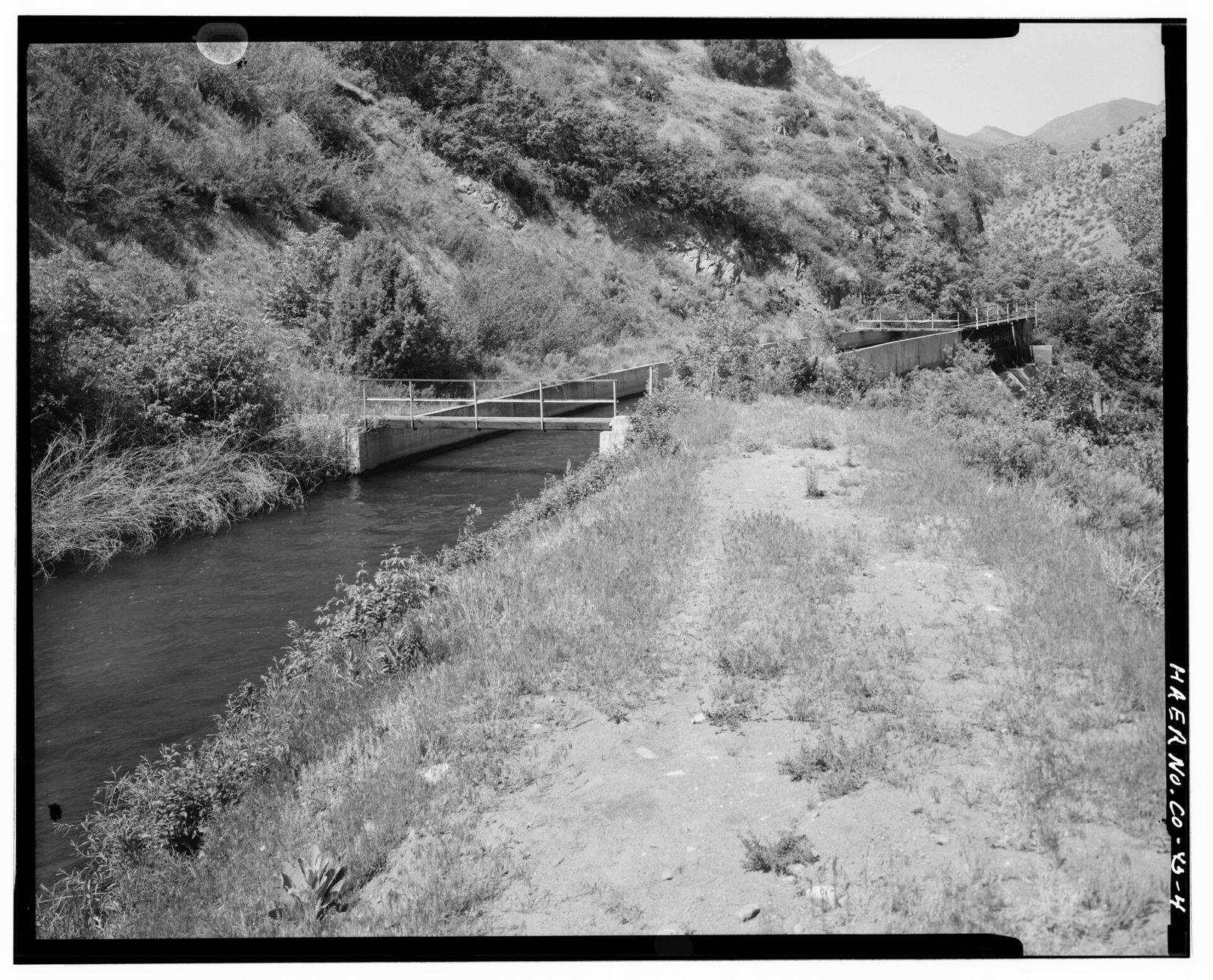 Canal exiting flume and beginning earth-lined main section at mouth of Platte river canyon. View to west.