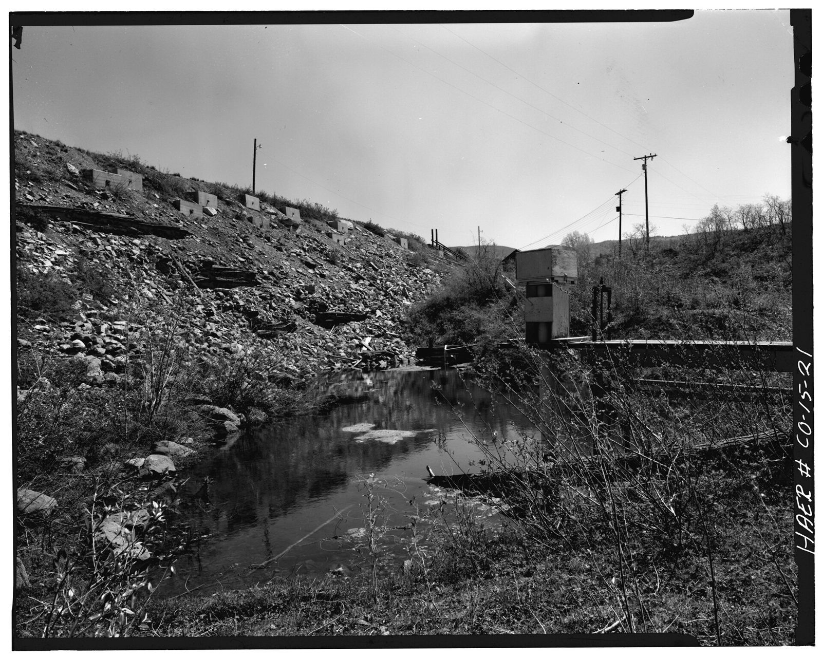 Side view; Downstream face of dam with seepage pond in foreground.