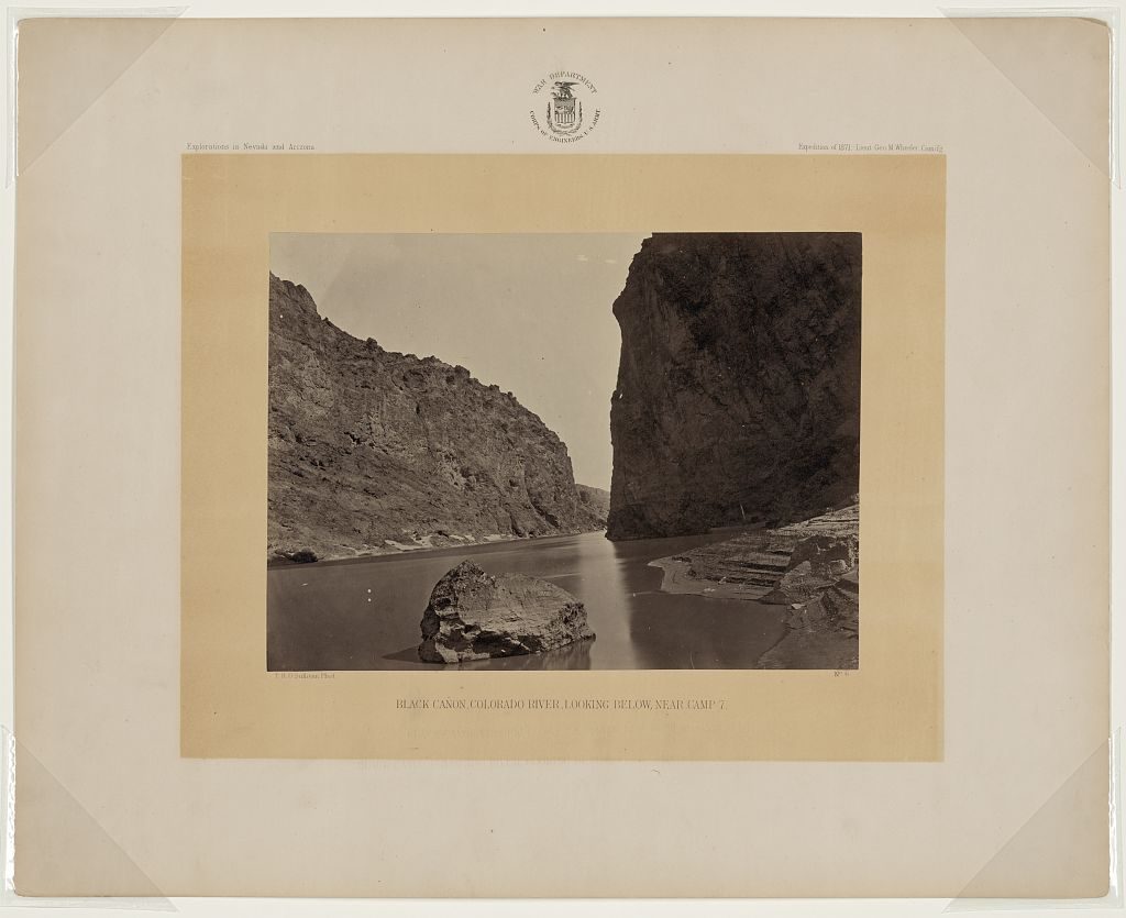 Dark canyon walls close in over a still river with a single pale boulder midstream; the albumen print is mounted under a War Department Corps of Engineers seal with its caption printed beneath.